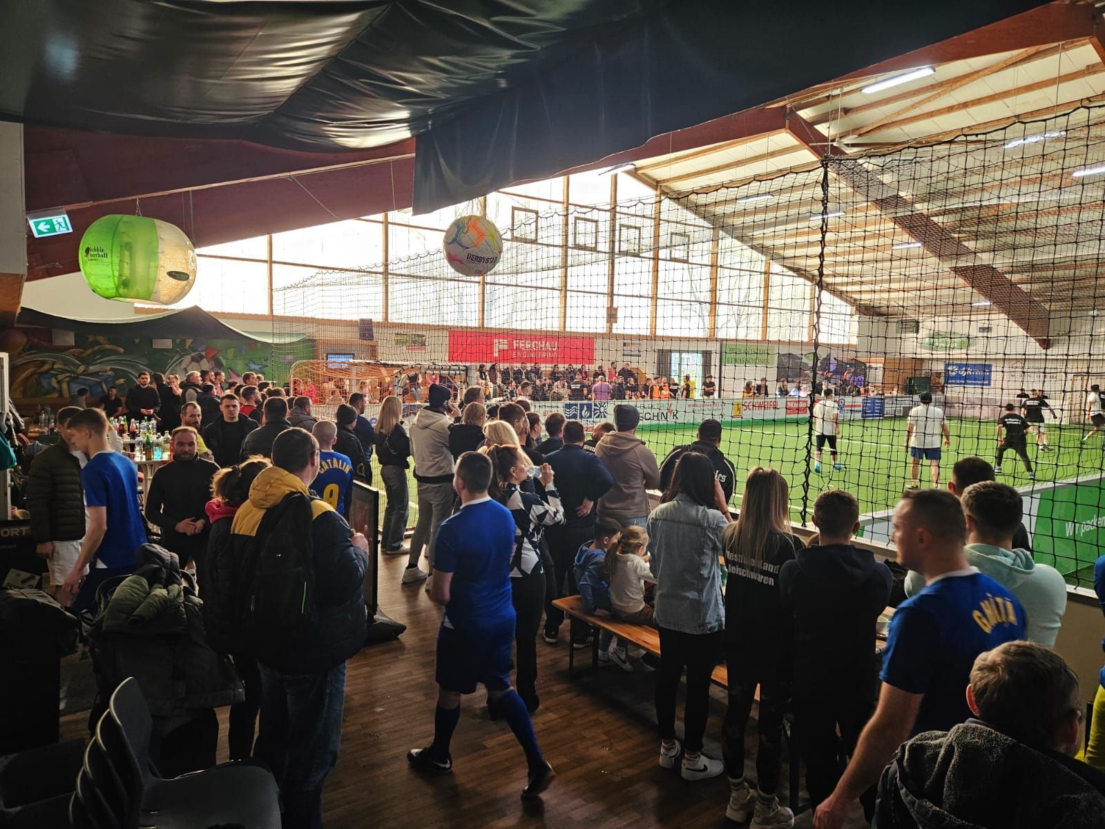 Eine große Gruppe von Menschen sieht sich in einem Hallenstadion ein Fußballspiel an.