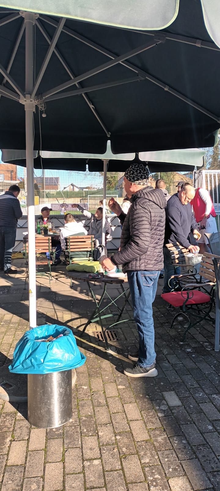 Eine Gruppe von Menschen steht unter Sonnenschirmen auf einer Terrasse.