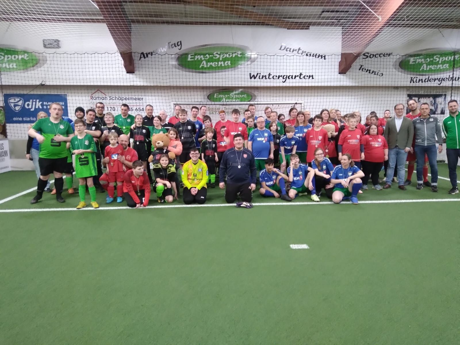 Gruppe von Menschen in Fußballtrikots posiert auf einem Hallenfeld.