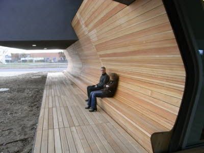 Zwei Personen sitzen auf einer Holzbank vor einer Holzwand.