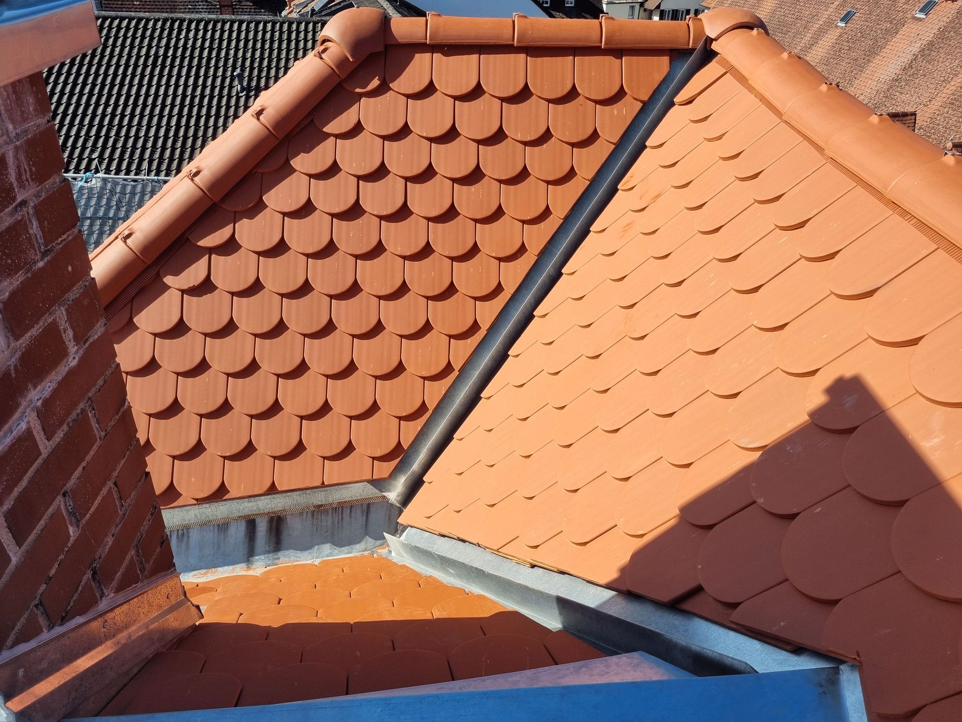 ein rotes Ziegeldach mit einem gemauerten Schornstein im Hintergrund