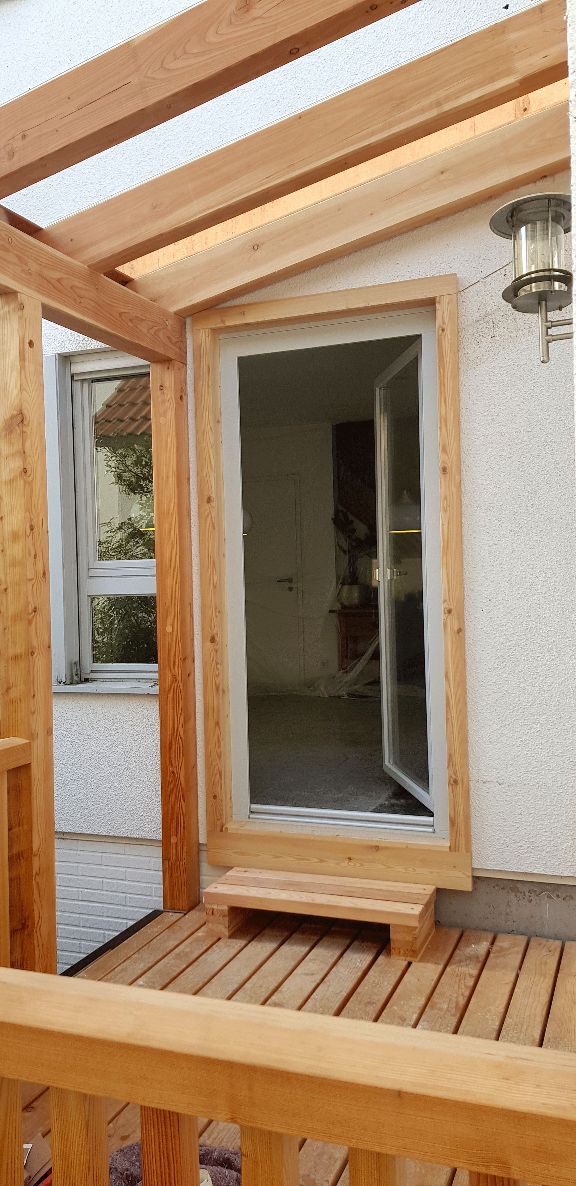 Eine Holzveranda mit einer Glasschiebetür und einem Fenster.