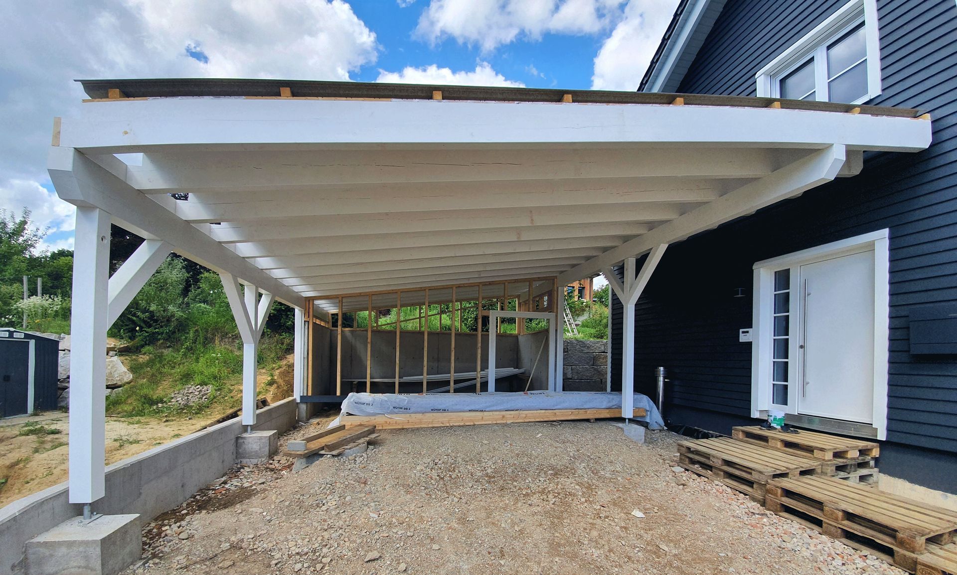 Vor einem schwarzen Haus wird ein Carport gebaut.