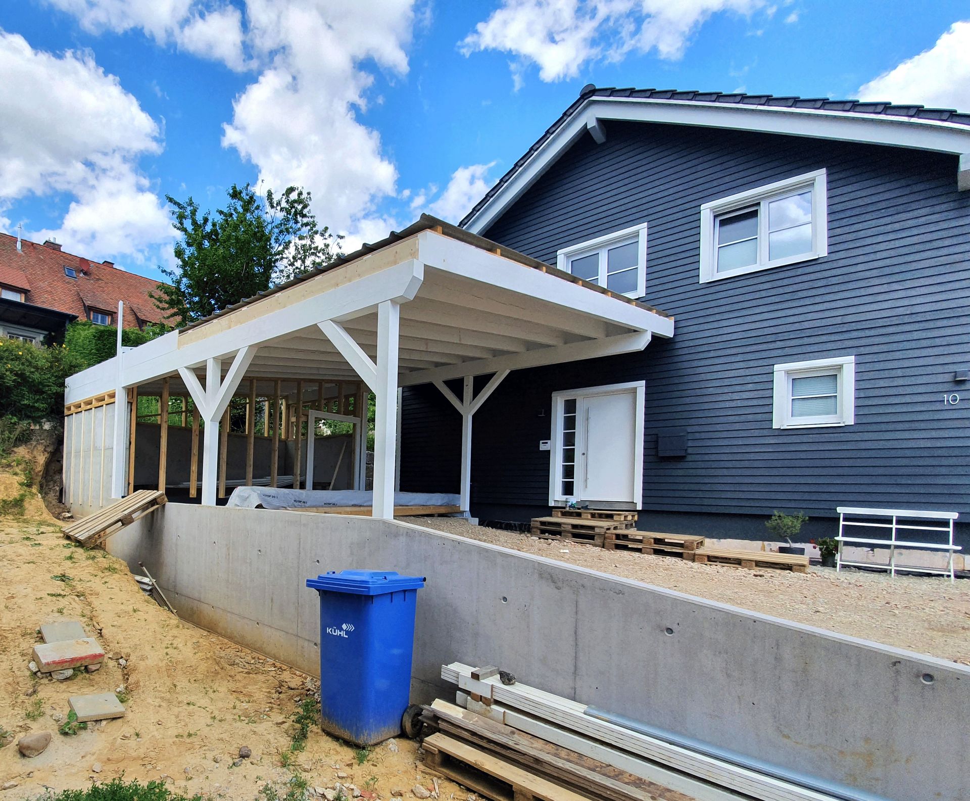 Ein blauer Mülleimer steht vor einem Haus im Bau