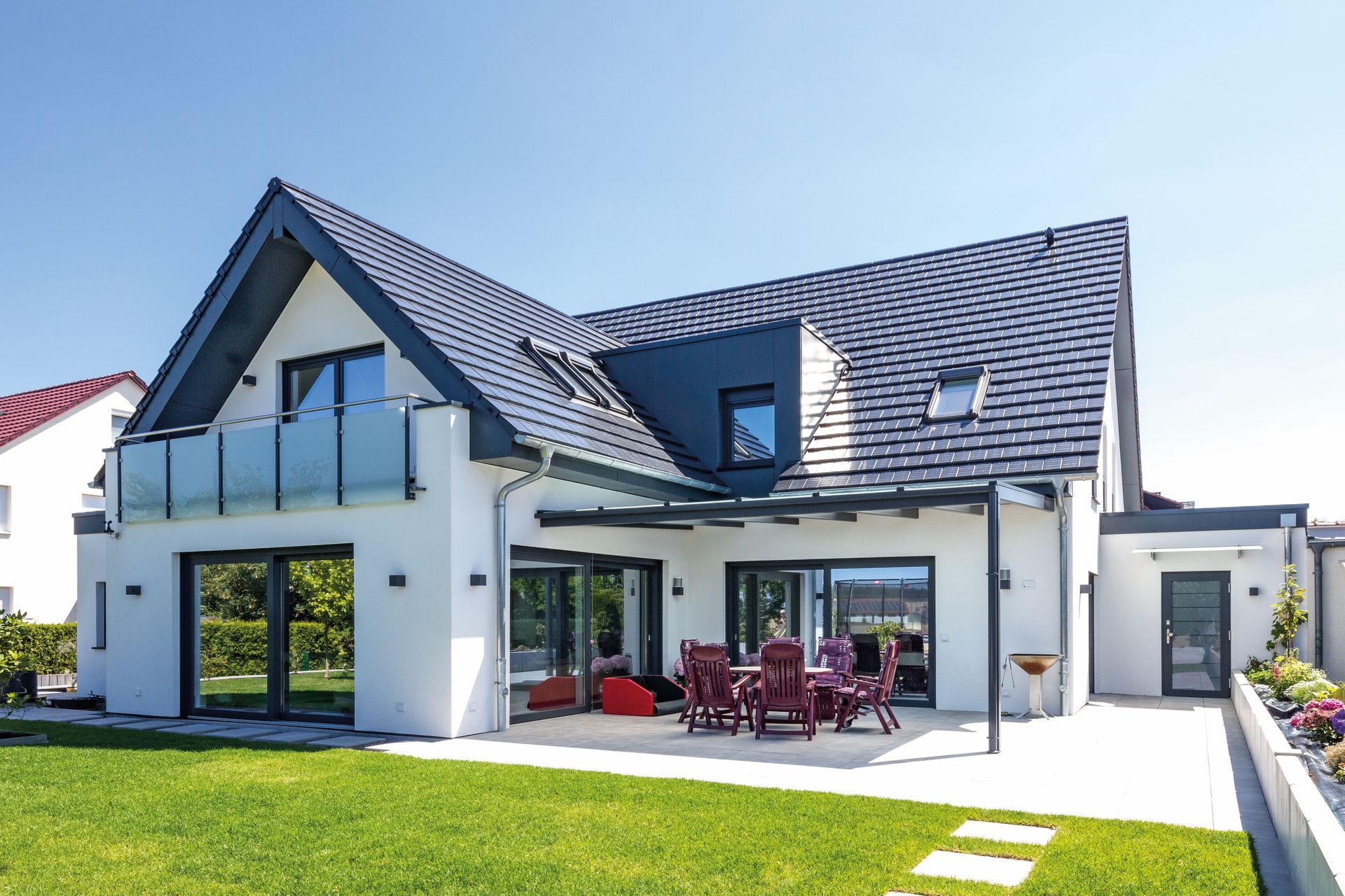 Ein großes weißes Haus mit schwarzem Dach und einer großen Wiese davor.