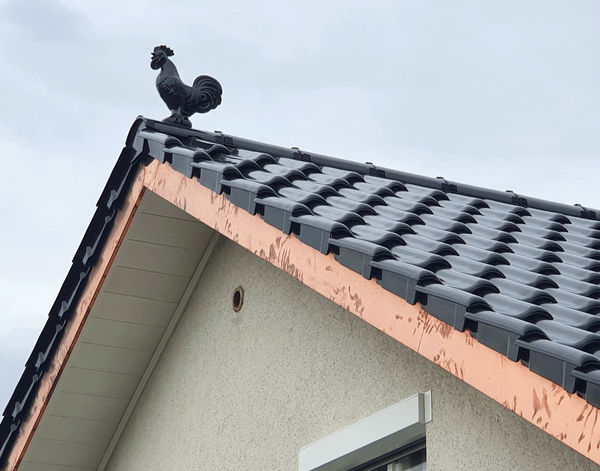 Auf dem Dach eines Hauses steht eine Hahnstatue.