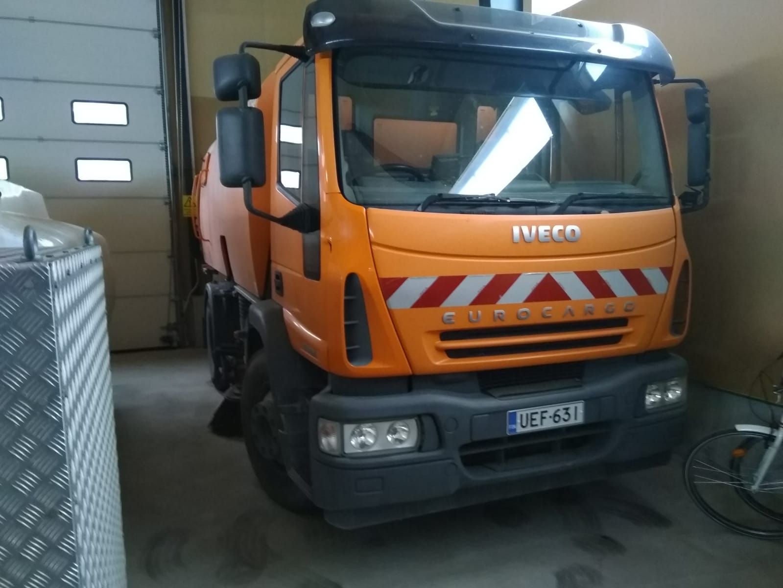 Oranssi Iveco-kuorma-auto pysäköitynä autotalliin, etunäkymä mustalla puskurilla ja raidoilla.