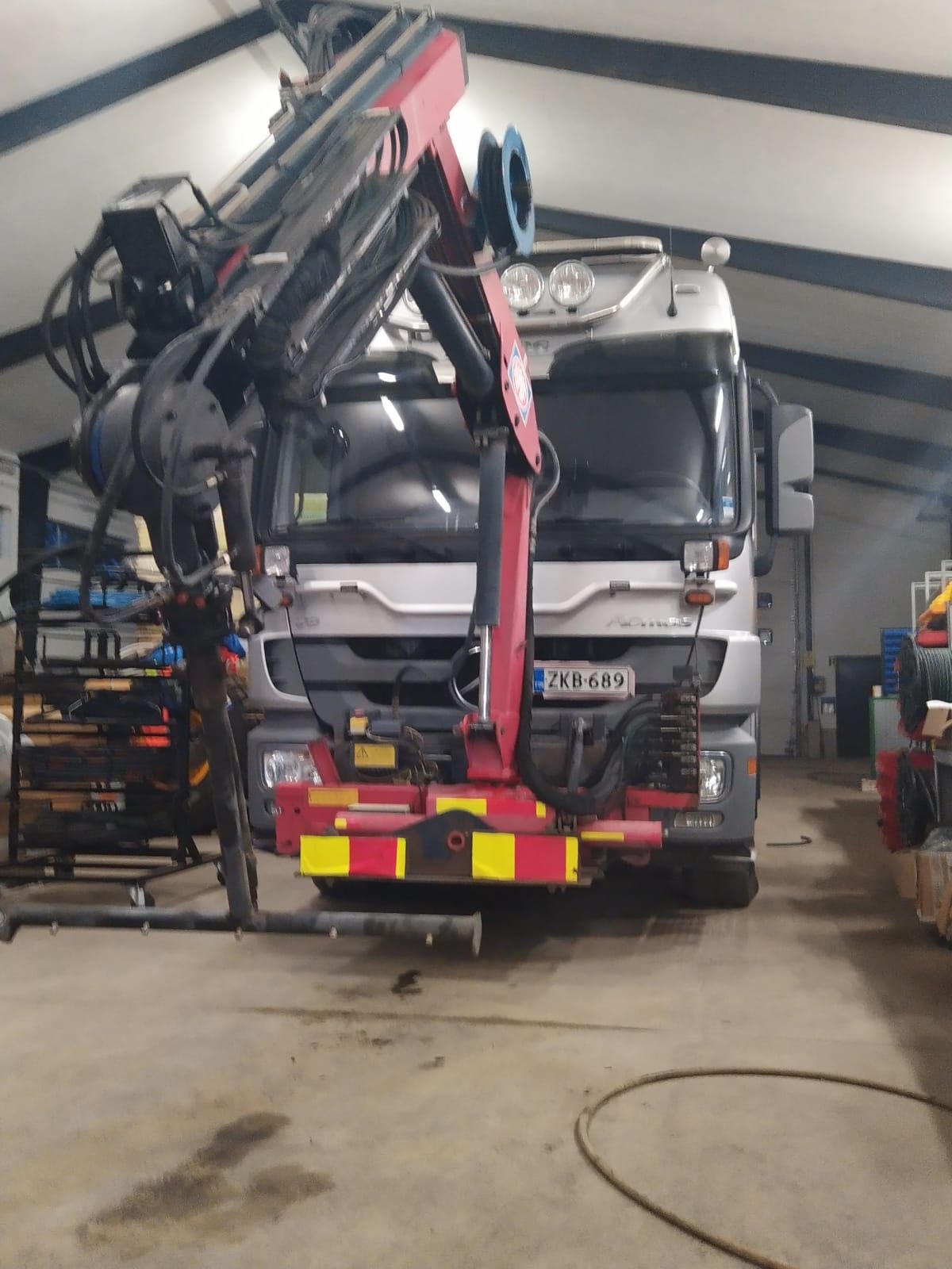 Punainen nosturiauto pysäköitynä sisätiloissa työpajassa, jossa on pidennetty puomi ja varusteet asennettuna takaosaan.