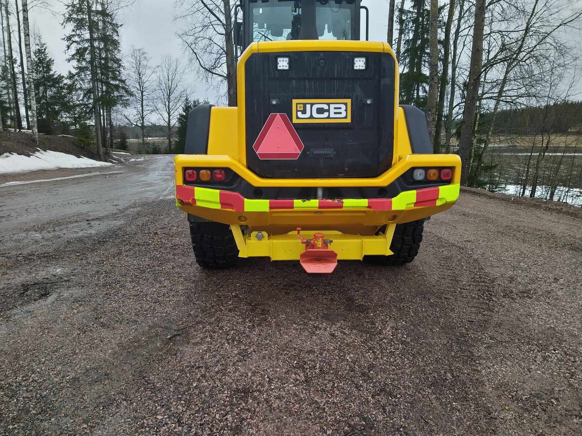 Keltainen JCB-työmaa-auto pysäköitynä soratielle lumisella, metsäisellä alueella