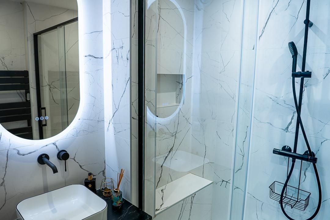 Salle de bains moderne avec miroirs rétroéclairés, murs en marbre blanc, lavabo et robinetterie de douche noire