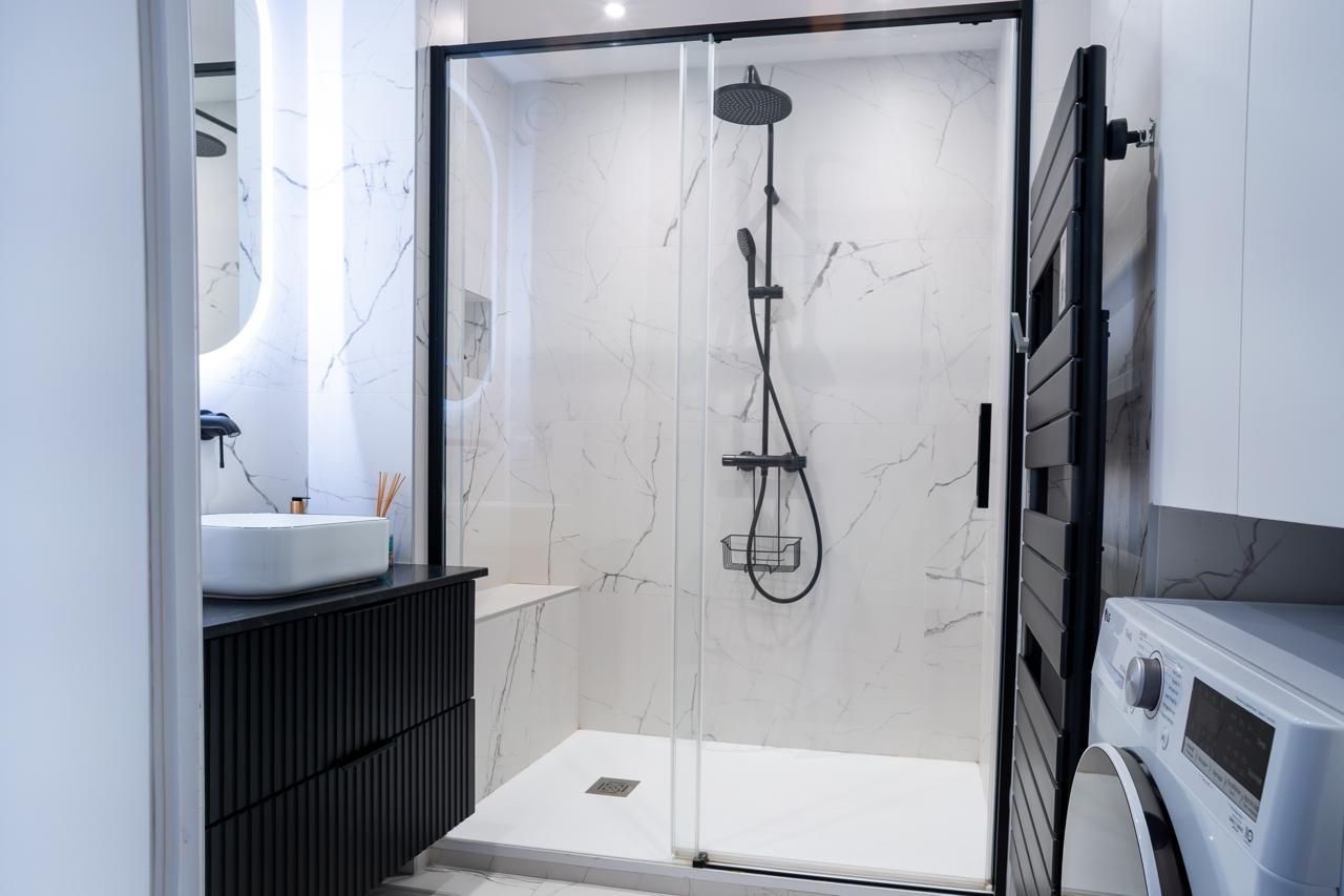 Salle de bains moderne avec douche en verre, murs en marbre blanc et robinetterie noire