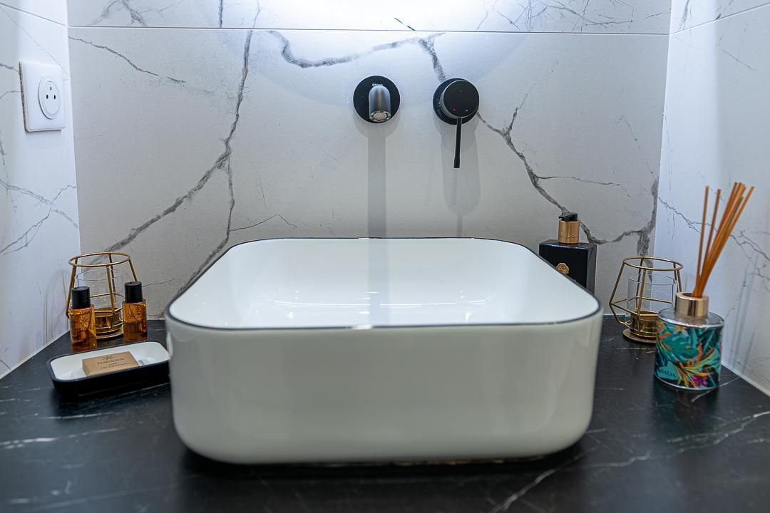Lavabo moderne avec deux robinets, vasque blanche, comptoir noir et porte-brosses à dents de chaque côté