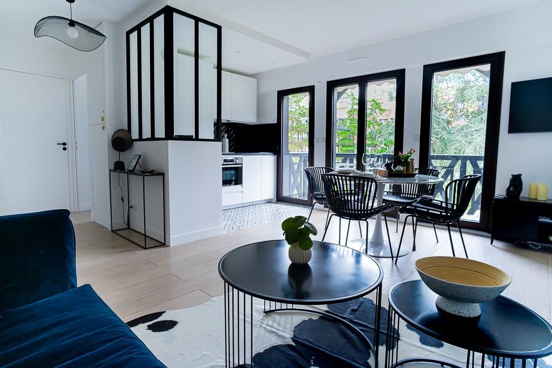Salon moderne avec des fenêtres à cadre noir, un canapé bleu, une table à manger et des plantes d’intérieur