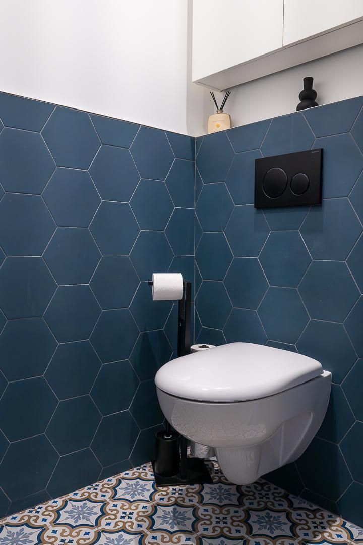 Coin de salle de bains carrelé de bleu, avec des toilettes suspendues, un porte-papier toilette et un sol à motifs