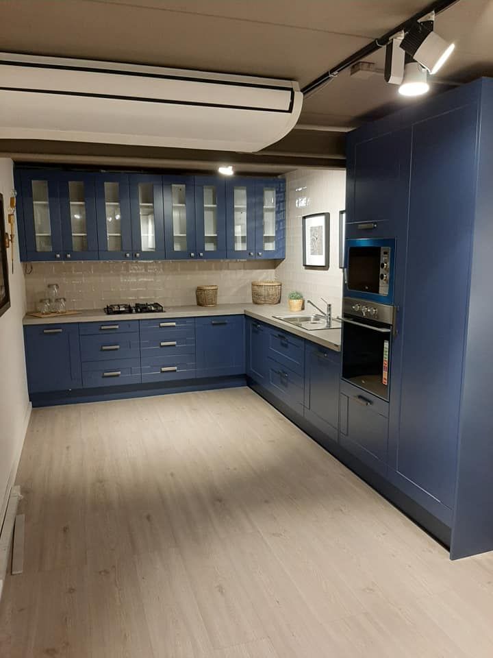 Gabinetes de cocina azules con encimeras y suelos claros. Incluye horno empotrado, placa de cocina y armarios superiores.