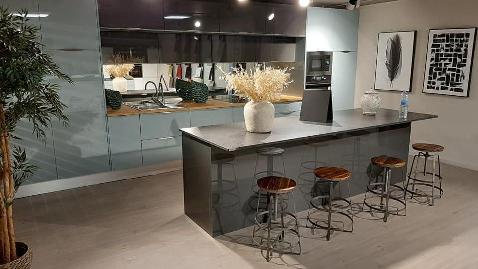 Cocina moderna con isla, muebles grises, taburetes de madera y elementos decorativos.