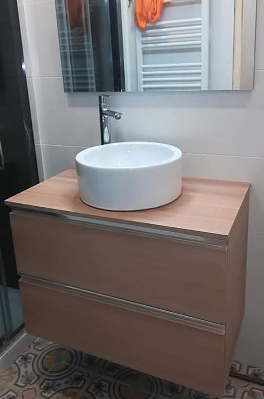 Mueble de baño con lavabo de vasija, mueble de madera clara, grifería cromada y espejo rectangular.