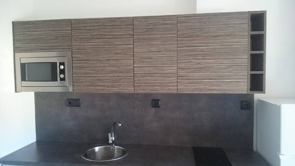 Muebles de cocina con microondas, fregadero y encimera. Muebles de madera color marrón grisáceo sobre un salpicadero gris oscuro.