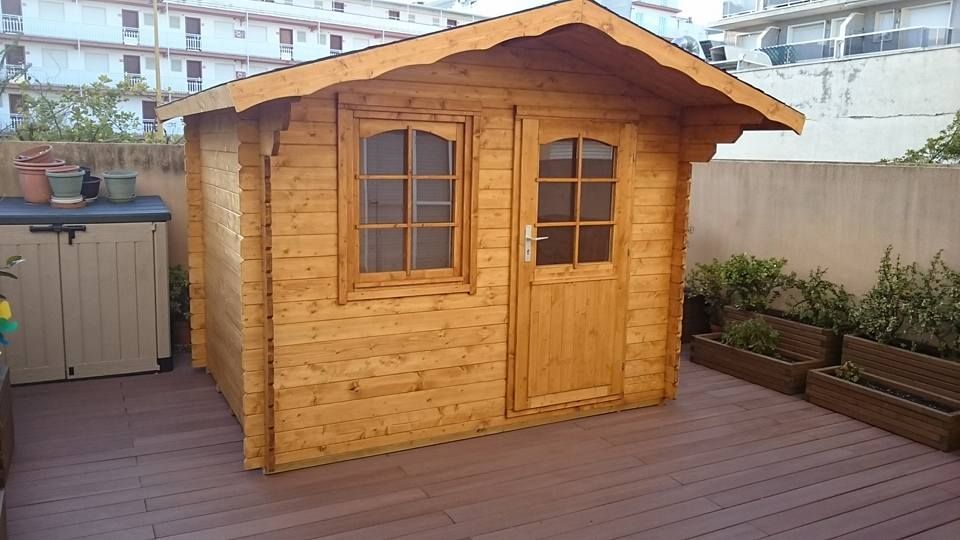 Cobertizo de jardín de madera con puerta y ventana sobre terraza de madera.