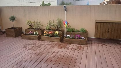 Jardineras de madera con flores de colores se encuentran en una terraza contra una pared.