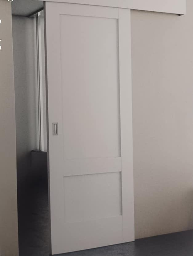 Puerta corrediza blanca en una pared de color claro, parcialmente abierta, revelando un espacio interior más oscuro.