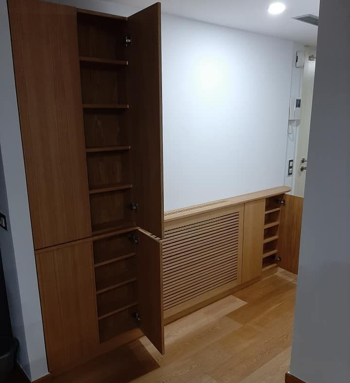 Armarios empotrados de madera con estantes. Un armario está abierto, dejando al descubierto el contenido. Paneles de madera y cubreradiador.
