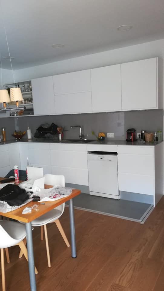 Cocina blanca moderna con pisos de madera, protector contra salpicaduras gris y una mesa de comedor.