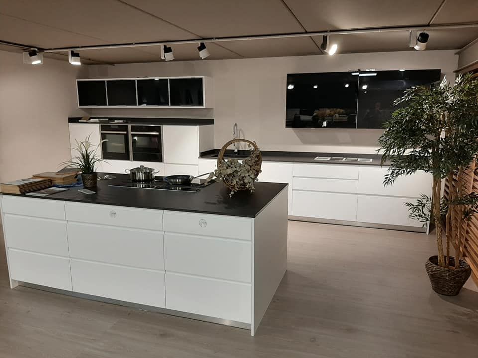 Cocina blanca moderna con encimeras y electrodomésticos negros, isla en el centro y un gran protector contra salpicaduras negro.