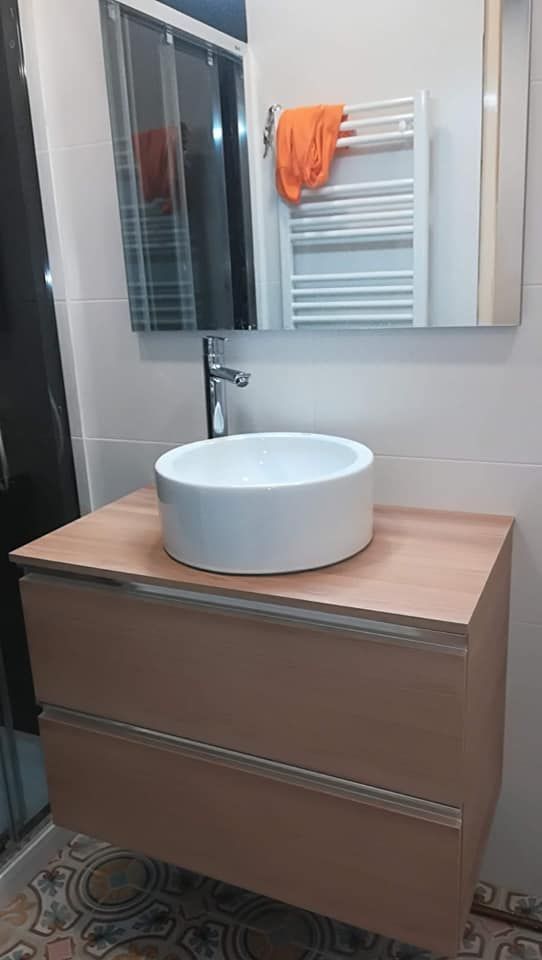 Baño con lavabo circular blanco sobre mueble de madera, con espejo y toallero.