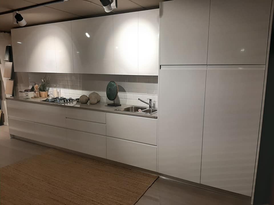 Cocina moderna blanca con gabinetes de alto brillo, encimera y fregadero.