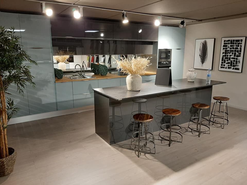 Cocina moderna con isla, taburetes y electrodomésticos; paredes azul claro, isla gris, arte y un árbol decorativo.