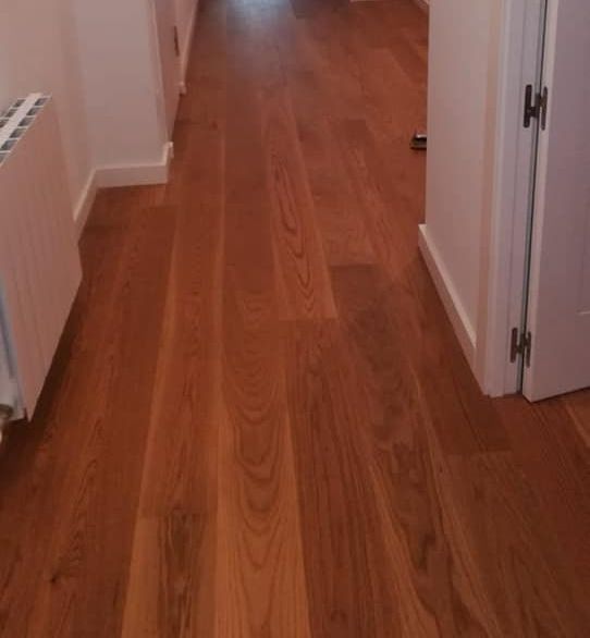 Suelo de madera en pasillo con paredes blancas y radiador.