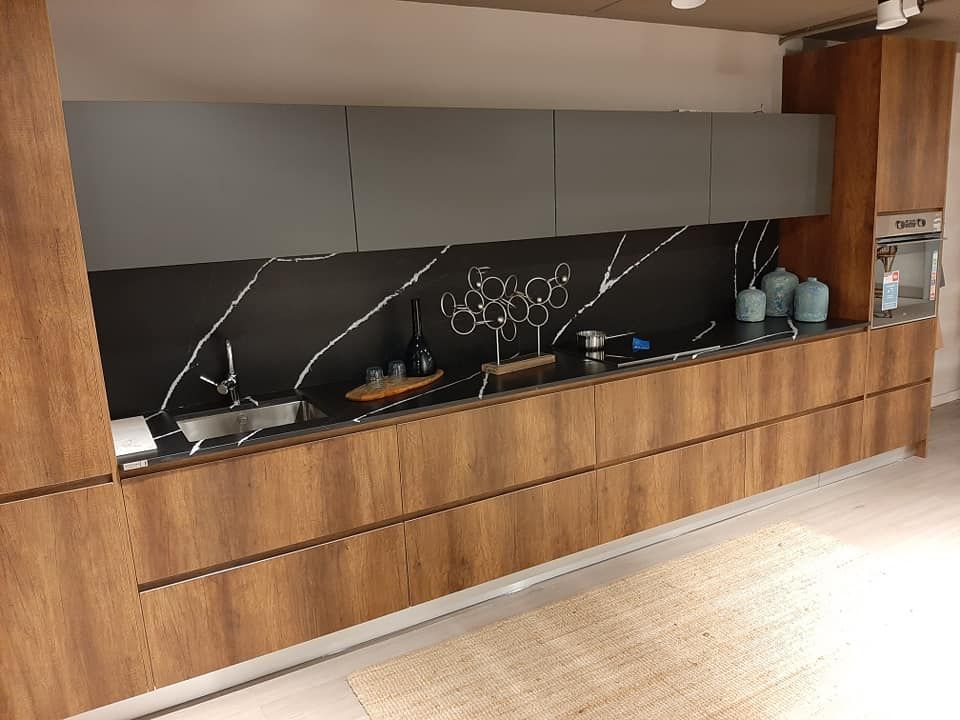 Cocina moderna con gabinetes de madera, gabinetes superiores grises y protector contra salpicaduras negro con vetas blancas.