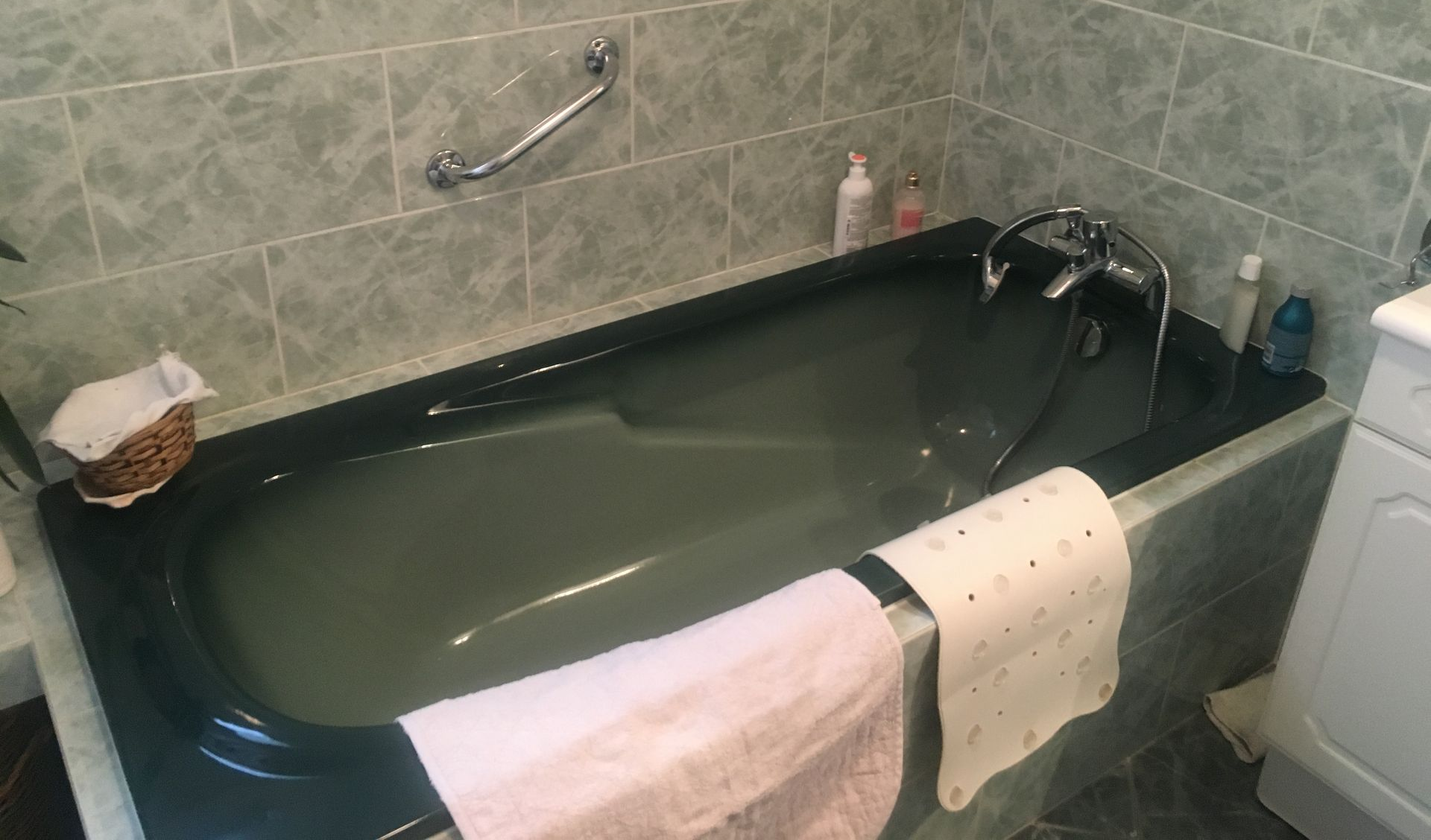 Une baignoire de couleur verte avec une poignée de maintien dans la salle de bains