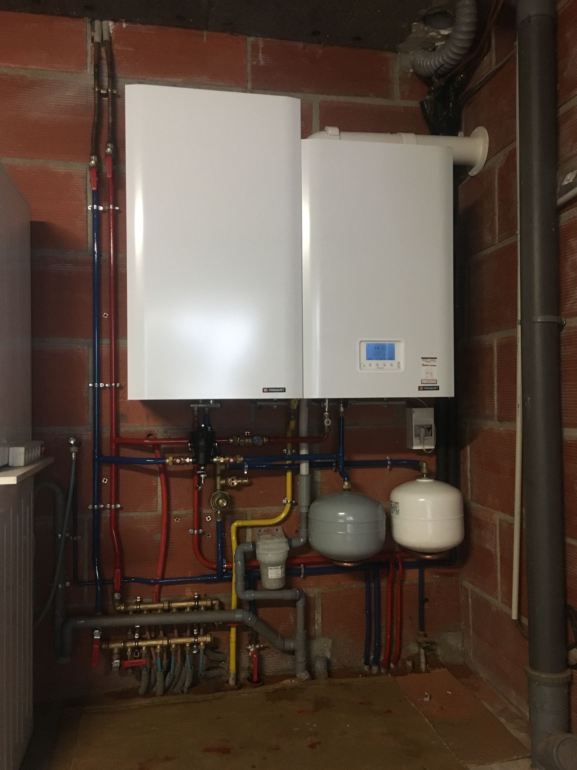 Deux unités de chauffage blanches fixées sur un mur en briques avec des tuyaux raccordés.