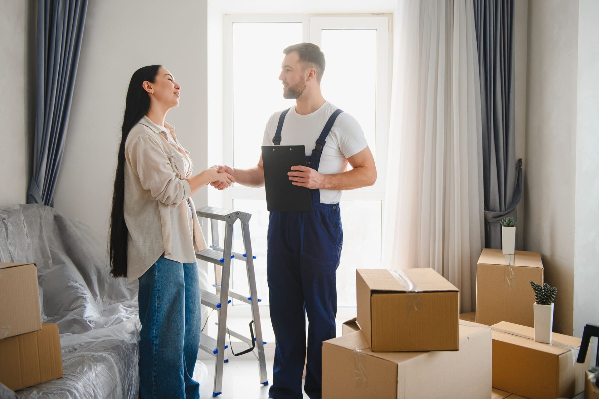 Una mujer estrecha la mano de un empleado de mudanzas en un apartamento con cajas de mudanza.