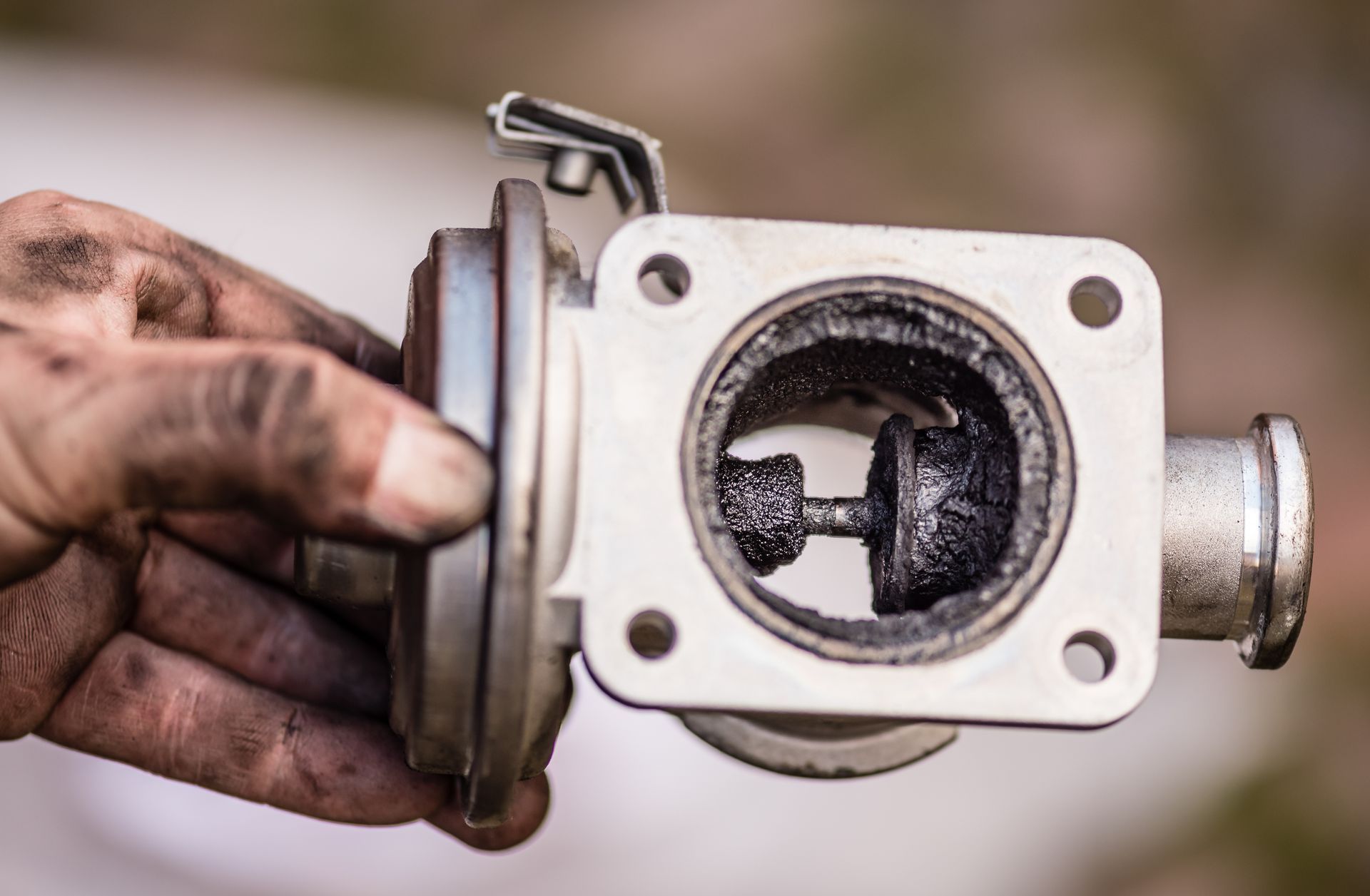 Une main sale tenant une pièce de moteur ou une valve métallique graisseuse, avec une ouverture circulaire et une bride