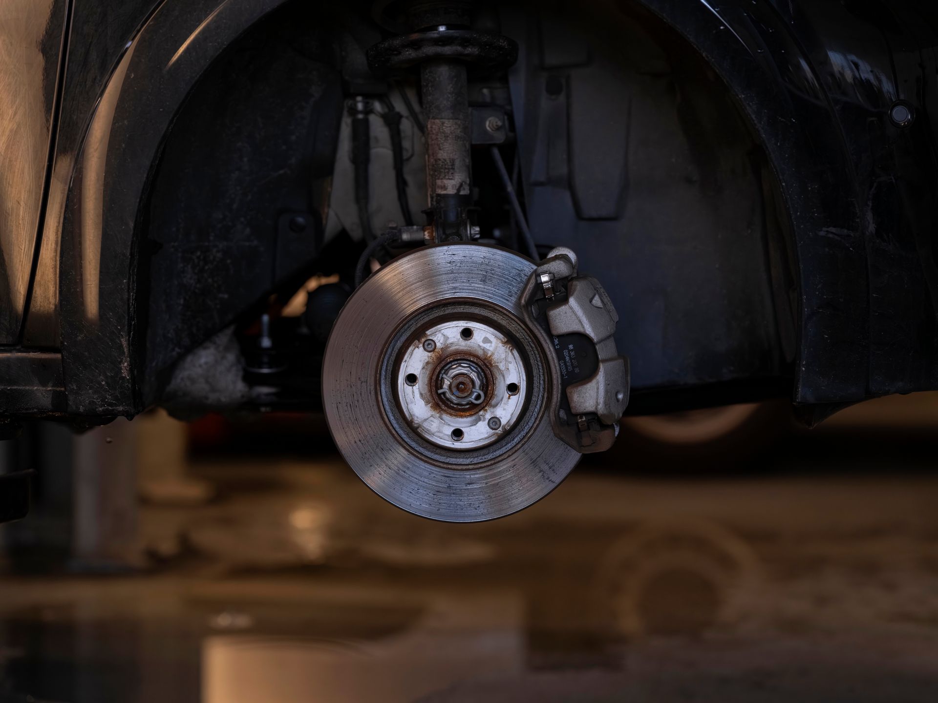 Roue de voiture et disque de frein dans un passage de roue sombre, la voiture étant soulevée du sol.