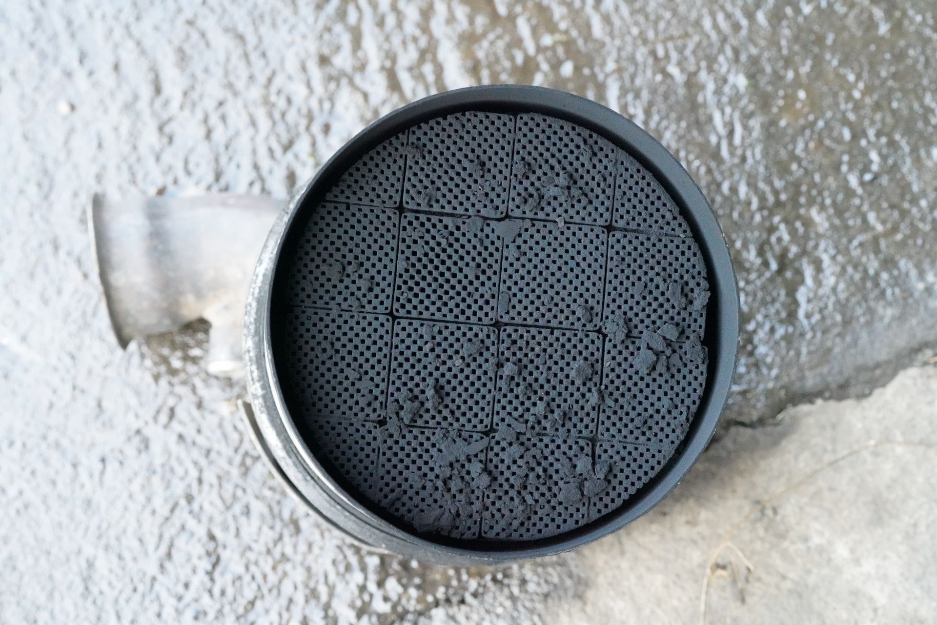 Ensemble de grilles d’aération rondes noires encastrées dans un mur en stuc blanc, avec un petit clapet à gauche