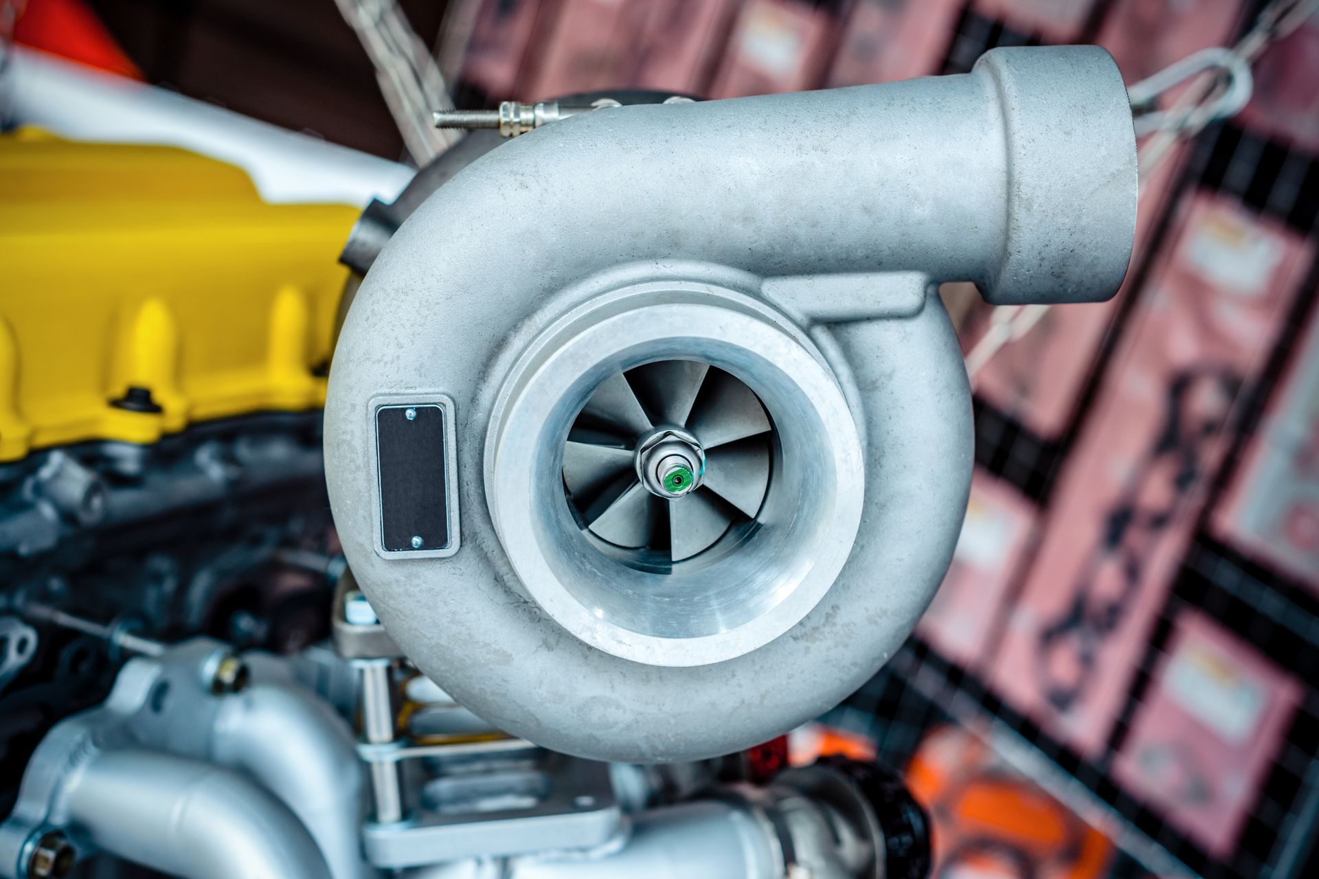 Gros plan d’un turbocompresseur argenté monté sur un moteur, avec des composants jaunes en arrière-plan