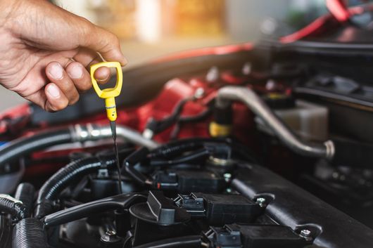 Une main tenant une jauge d’huile jaune au-dessus du compartiment moteur d’une voiture