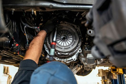Mécanicien travaillant sous une voiture sur un pont élévateur et installant une boîte de vitesses ou un embrayage
