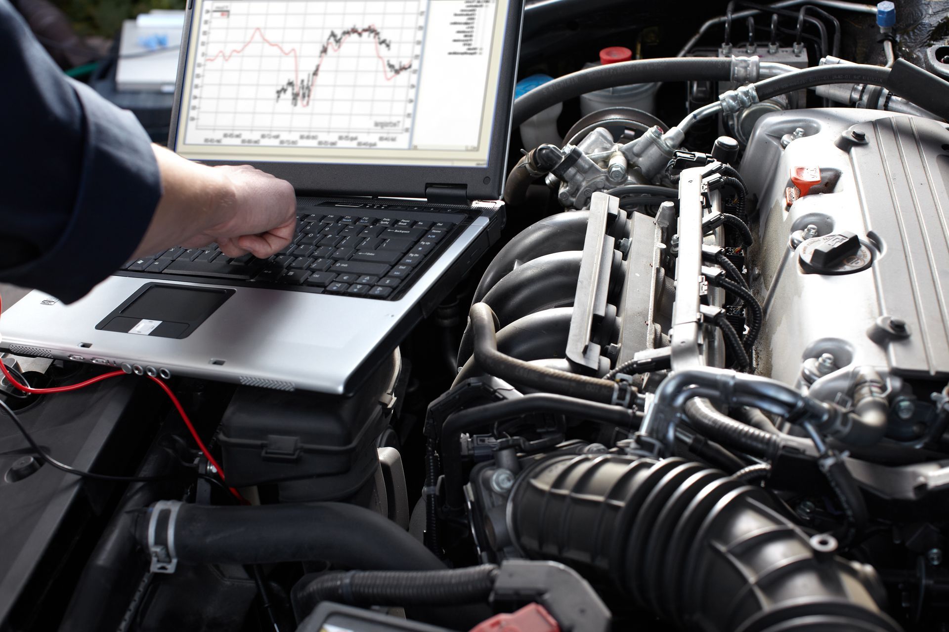 Un mécanicien utilise un ordinateur portable pour diagnostiquer le moteur d’une voiture dont le capot est ouvert