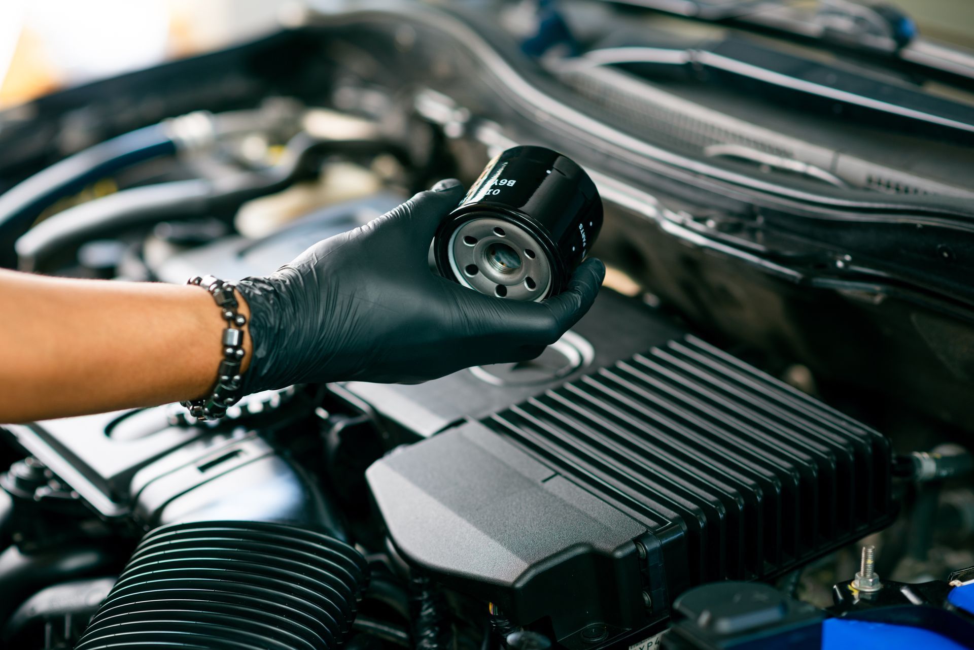 Une main gantée tenant un filtre à huile au-dessus du compartiment moteur d’une voiture