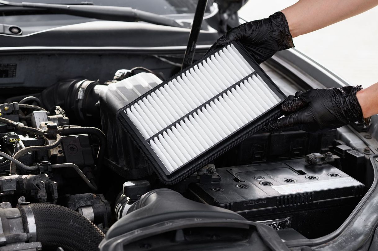 Des mains gantées installent un filtre à air neuf dans le compartiment moteur d’une voiture