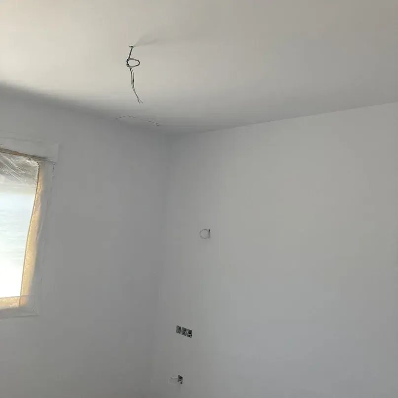 Una habitación con paredes blancas y una ventana con cables colgando del techo.