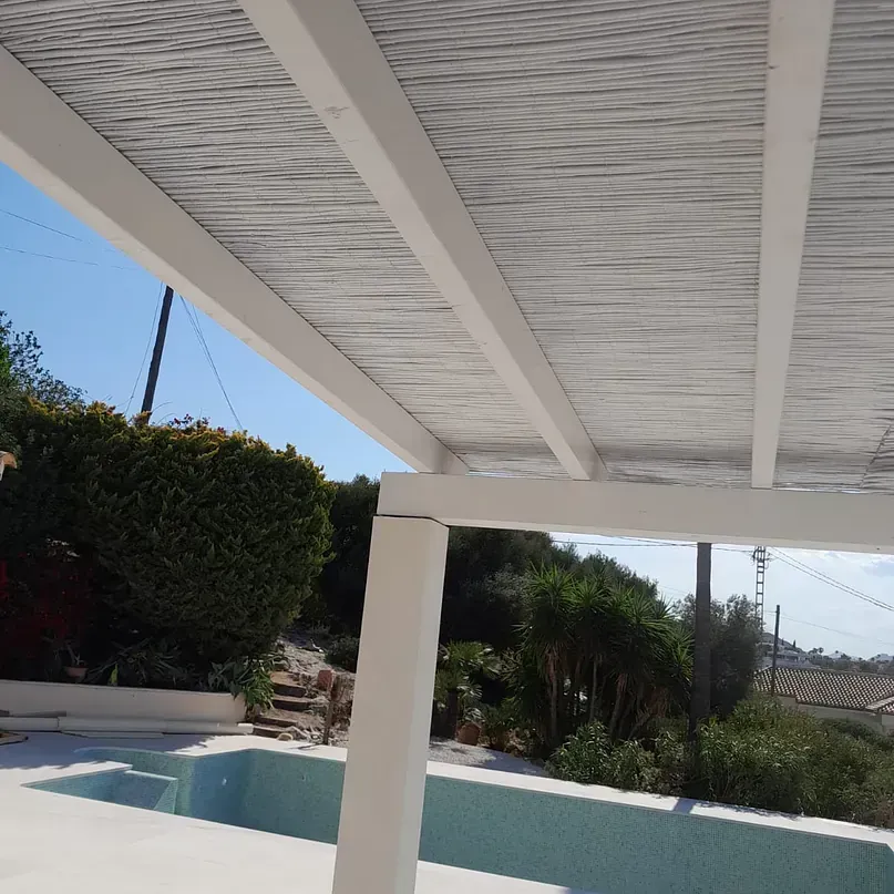 Una pérgola blanca con vistas a una piscina con árboles al fondo.