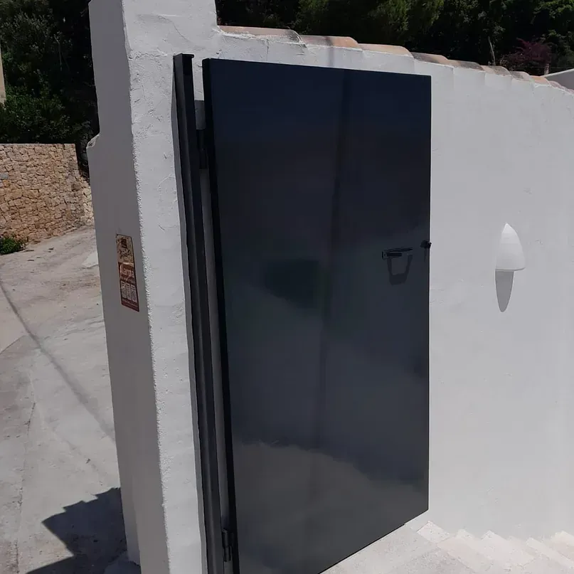 Una puerta negra está sentada al costado de una pared blanca.