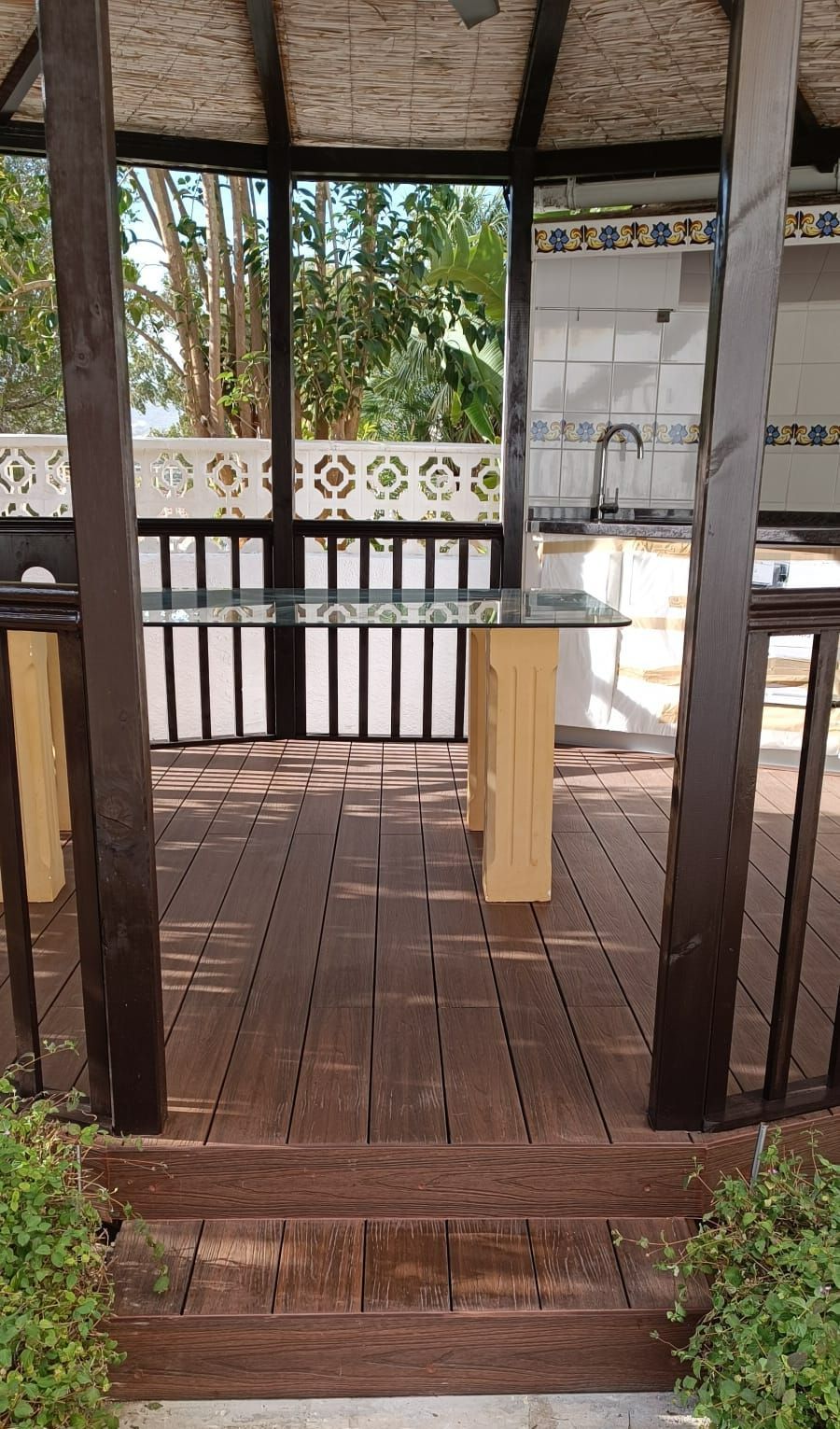 Una terraza de madera con una mesa y sillas debajo de un cenador.