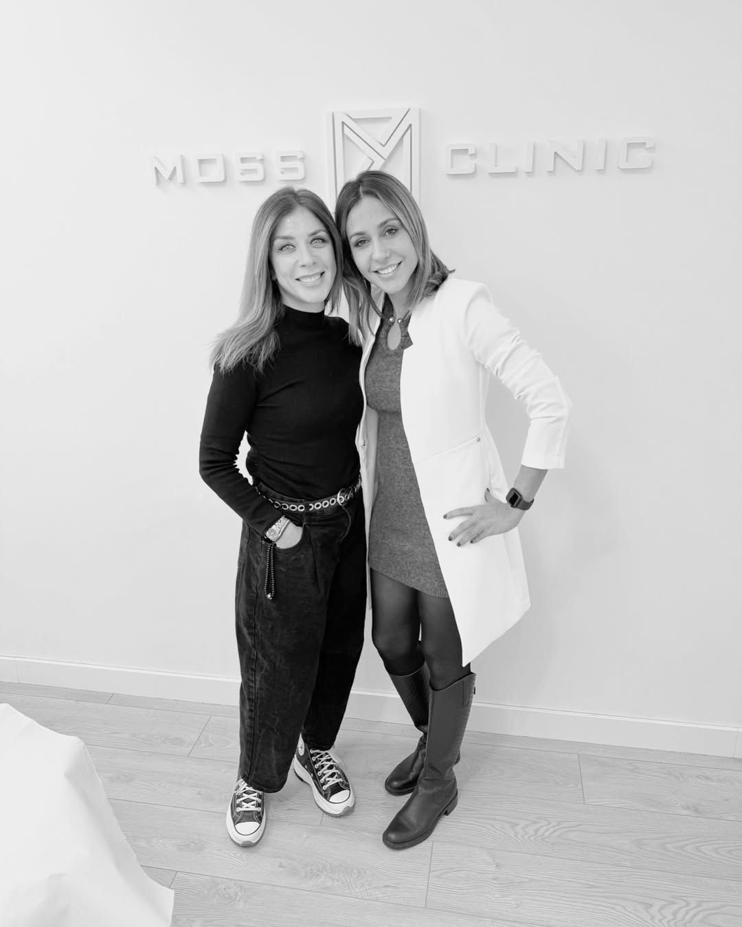 Dos mujeres posan para una foto frente a una pared que dice Clínica de Alces.